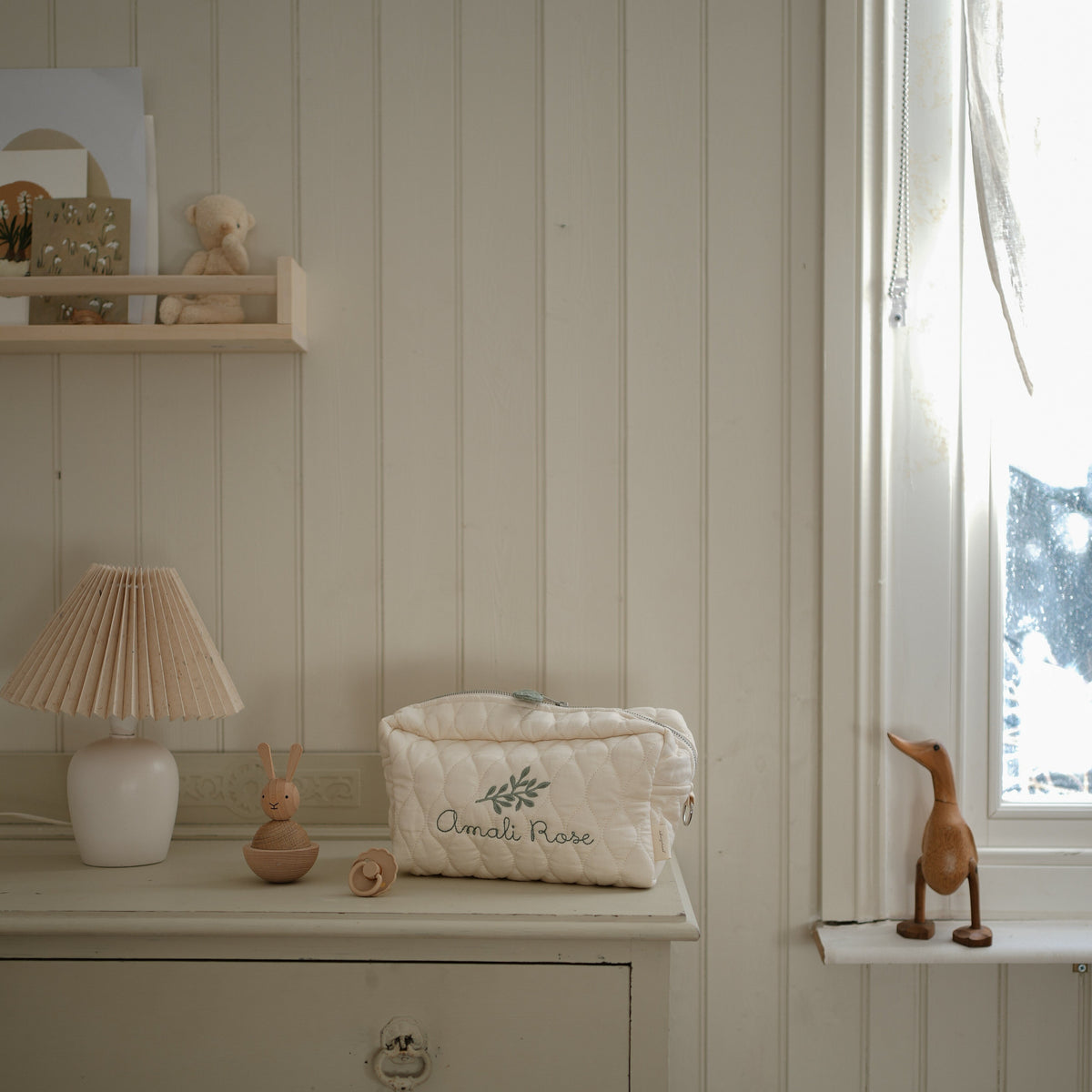 Toiletry Pouch in Ivory sitting on top pf dresser with pacifier, lamp and toys near by