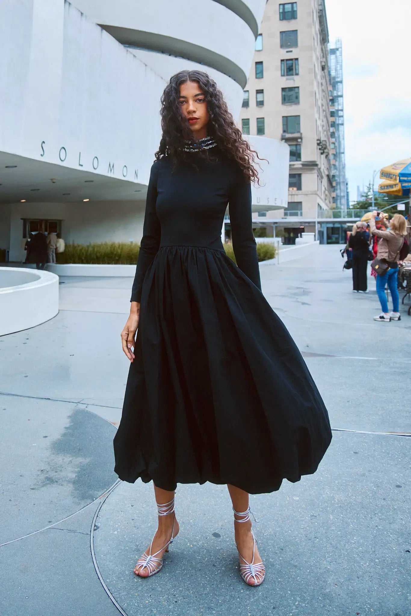 The Alexandra Dress is a fitted bodice with long sleeves, bubble skirt, and jeweled trim neckline. 