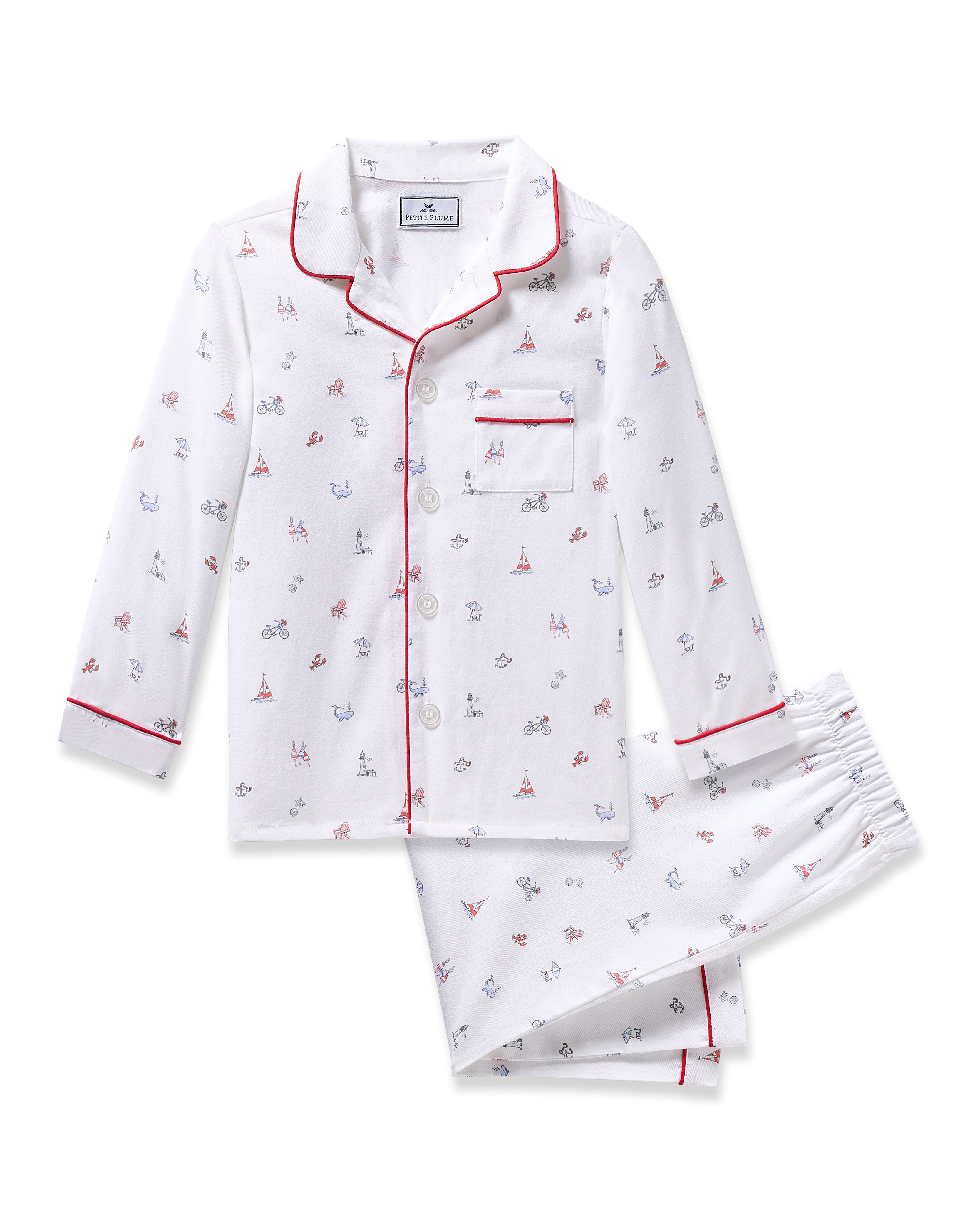 The Kids Twill Pajama in Coastal Charms by Petite Plume is flame-retardant, made from yarn-dyed cotton, and features a white design with red piping, adorned with small bicycle and Eiffel Tower prints. It includes a long-sleeve button-up top with a chest pocket and matching pants.