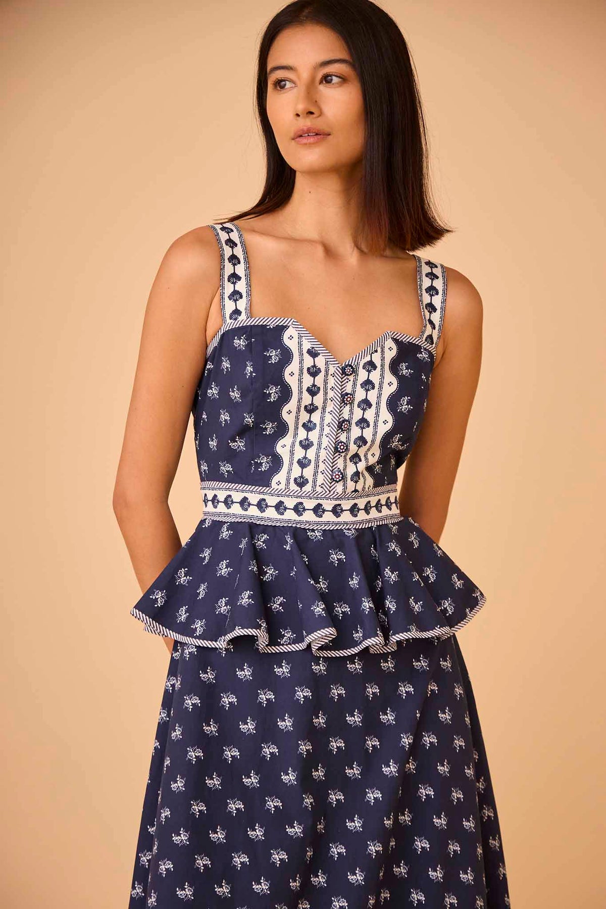 The Lacey Dress has a sweetheart neckline, a fitted bodice, peplum hem, and painted flower buttons.