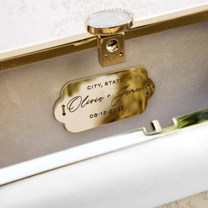 Two names and a date engraved on the Personalized Plaque Sentiment Engraving attached to a cream-colored Bella Rosa bag, suggesting a personalized accessory for a special occasion from The Bella Rosa Collection.