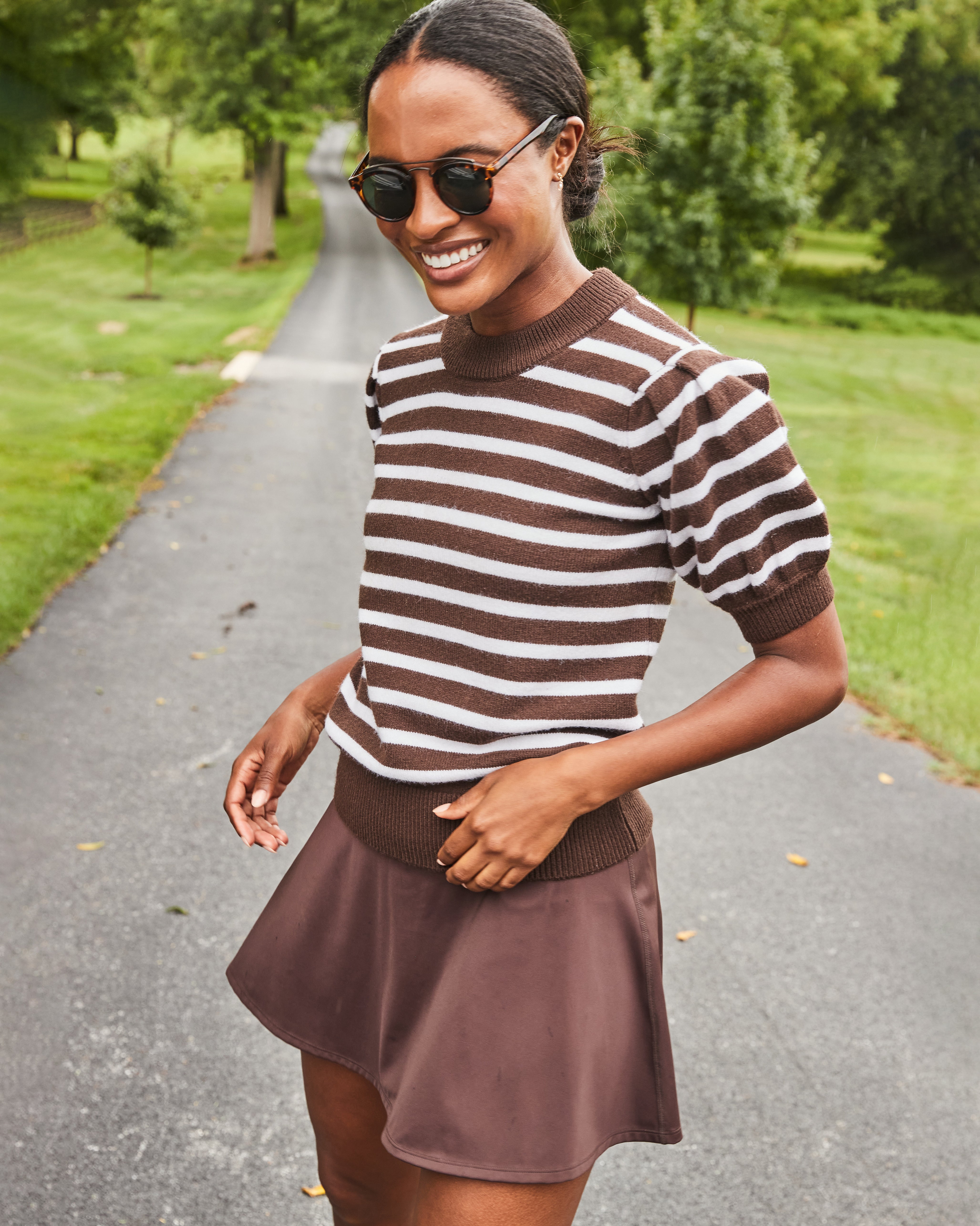 Model is wearing the Locust Active Sweater in Chocolate/ Off White Stripe with the Flounce Skort in Chocolate