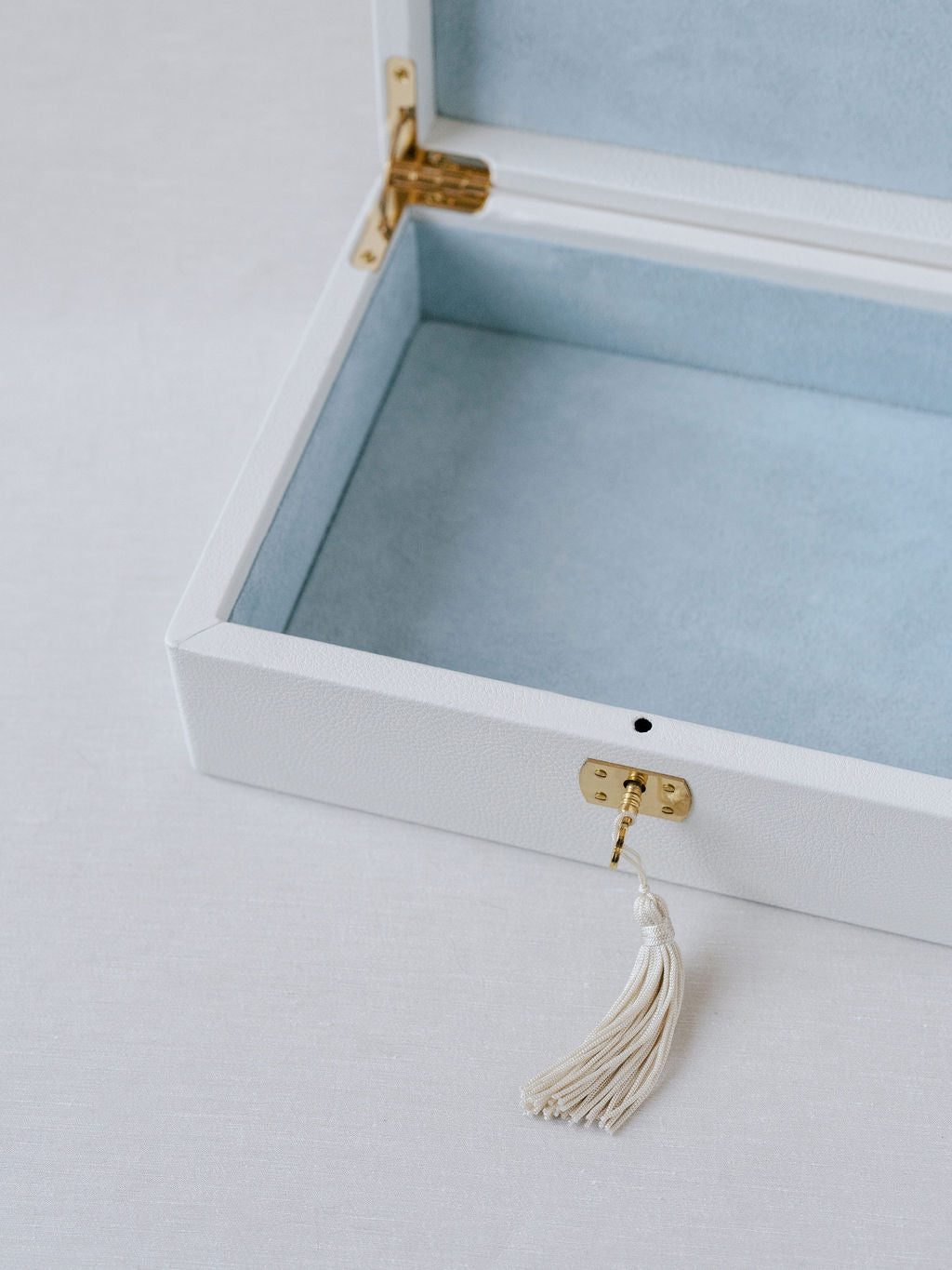 Close up image of the white Italian leather wedding keepsake box. Shown is the gold accented key with tassel inserted into the key hold. Box is open with blue suede interior and can hold all wedding day mementos.