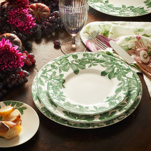 A vintage romance table setting featuring Caskata Arbor Green Dinner Plates with a green border, complemented by a cluster of grapes as an elegant centerpiece.